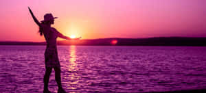 A Woman Is Standing On A Dock At Sunset Wallpaper