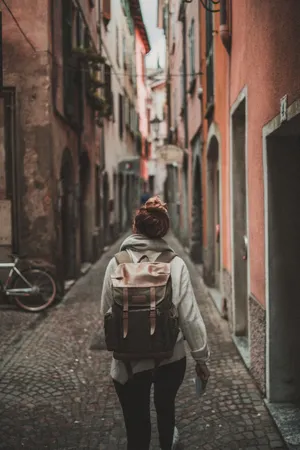 A Woman Walking Down A Narrow Street With A Backpack Wallpaper