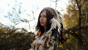 A Woman Wearing A Feathered Headdress In The Forest Wallpaper