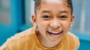 A Young Girl Is Smiling While Sitting On A Chair Wallpaper