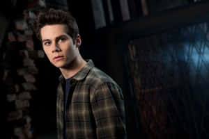 A Young Man In A Plaid Shirt Is Standing In Front Of A Brick Wall Wallpaper