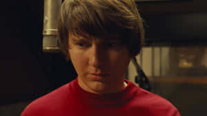 A Young Man In A Red Shirt Is Standing In Front Of A Microphone Wallpaper