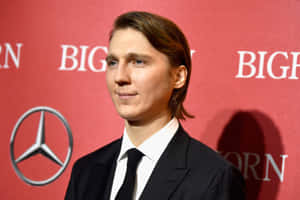 A Young Man In A Suit And Tie Standing In Front Of A Red Wall Wallpaper