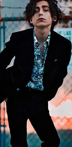 A Young Man In A Suit Leaning Against A Fence Wallpaper