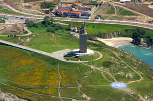 Aerial View Of The Majestic Tower Of Hercules Surrounded By Lush Green Grass Wallpaper