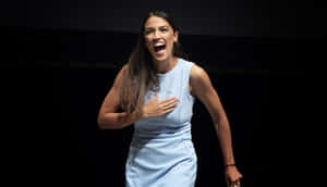 Alexandria Ocasio-cortez In Blue With Black Backdrop Wallpaper