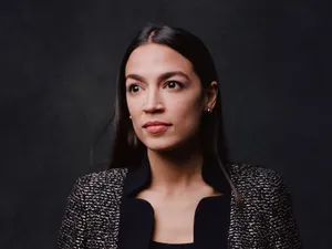 Alexandria Ocasio-cortez Posing Against A Black Backdrop Wallpaper