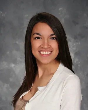 Alexandria Ocasio-cortez Smiling With Gray Backdrop Wallpaper