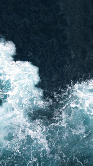 An Aerial View Of The Power Of Ocean Waves Crashing Against The Shore. Wallpaper