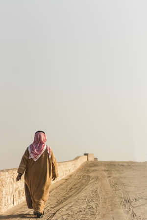 An Arab Man Peacefully Walking Along A Desert Road Wallpaper