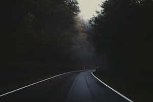 An Eerie Dark Road Illuminated By Moonlight Wallpaper