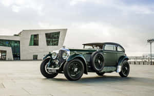 An Old Green Car Parked In Front Of A Building Wallpaper