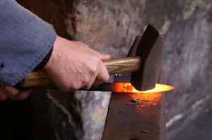 An Old-time Blacksmith Works Away At His Anvil Wallpaper