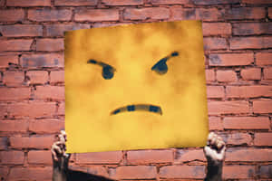 Angry Face Placard Against Brick Wall Wallpaper