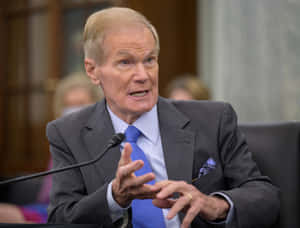 Bill Nelson Dressed In A Gray Suit With A Blue Tie. Wallpaper