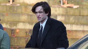 Bruce Wayne Standing In The Darkness With A Stern Gaze And Bat Signal Behind Him Wallpaper