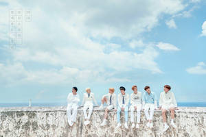 Bts Sitting On Stone Border Under Sky Wallpaper