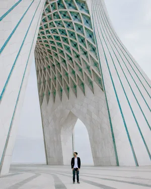 Caption: Man Standing In Front Of The Azadi Tower In Tehran, Iran Wallpaper