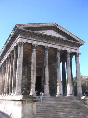 Caption: Person Ascending Steps Of The Historic Maison Carrée Wallpaper