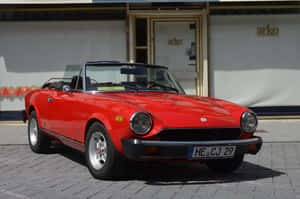 Caption: Stunning Red Fiat 124 Spider Cruising In Style Wallpaper