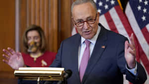 Chuck Schumer Speakingwith American Flag Background Wallpaper