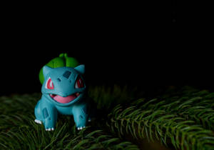 Cuddly Bulbasaur Toy Enjoying A Snack In The Pine Forest Wallpaper