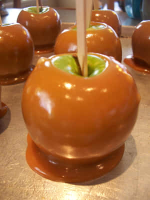 Delectable Caramel Apples On A Wood Table Wallpaper