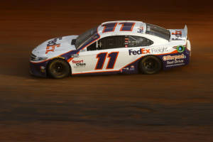 Denny Hamlin Skillfully Navigates Dirt Road In A High-speed Race Wallpaper