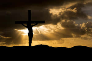 Depiction Of Christ's Crucifixion On A Cross Against A Dramatic Sky Wallpaper