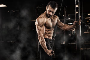 Determined Muscle Man Performing Single Arm Tricep Pushdown Wallpaper