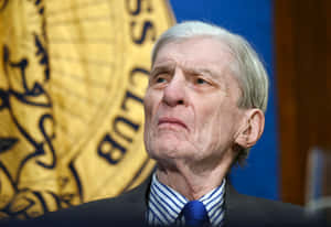 Distinguished John Warner Posing Before Blue Backdrop Wallpaper