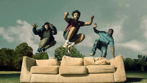 Donald Gloverand Friends Jumping Over Couch Outdoors Wallpaper