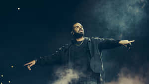 Drake Is Standing On Stage With His Arms Outstretched Wallpaper