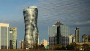 Dusk Falls Over The Bustling Cityscape Of Mississauga With Illuminated Skyscrapers Mirrored On The Lake's Surface Wallpaper