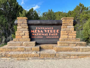 Entrance Sign Of Mesa Verde National Park Nestled Amidst Lush Greenery Wallpaper