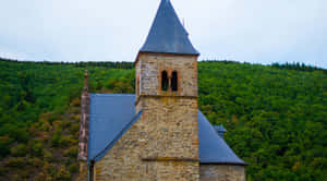 Eschsur Alzette_ Church_ Against_ Forest_ Backdrop Wallpaper