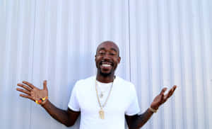 Freddie Gibbs Smiling Against Metal Wall Wallpaper