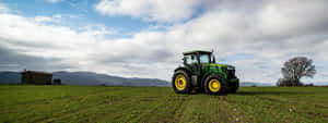 Green_ Tractor_in_ Field_with_ Mountain_ Backdrop Wallpaper