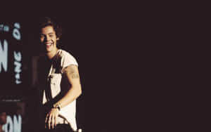 Harry Styles Looking Content As He Types On His Laptop Wallpaper