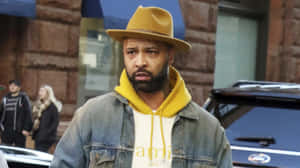 Joe Budden Wearing Yellow Hoodieand Brown Hat Wallpaper