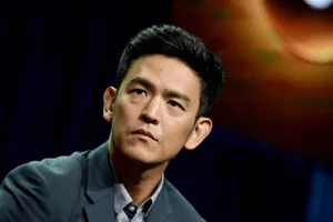 John Cho Smiling In A Stylish Outfit Against A Blue Background Wallpaper