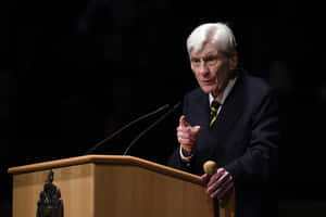 John Warner On A Podium With Black Backdrop Wallpaper