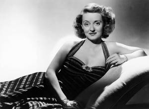 Legendary Bette Davis Relaxing On A Couch Wallpaper