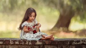 Little Girl Playing Ukulele Outdoors Wallpaper