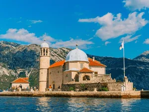 Majestic Our Lady Of The Rocks Church Against A Scenic Mountain Backdrop Wallpaper