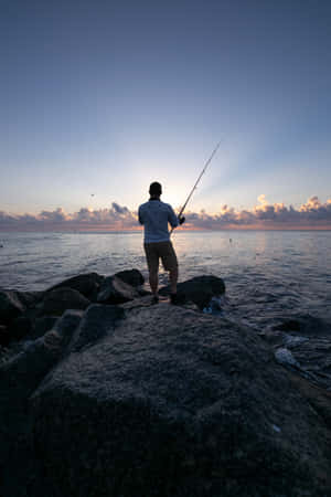 Man Fishing By The Lake Using His Phone Wallpaper