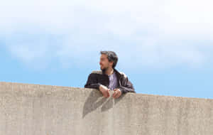 Man Leaningon Wall Under Blue Sky Wallpaper