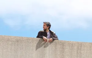 Man Leaningon Wall Under Blue Sky Wallpaper