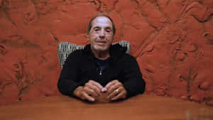 Man Seated Against Red Textured Wall Wallpaper