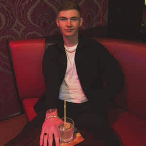 Man Seatedin Red Boothwith Drink Wallpaper